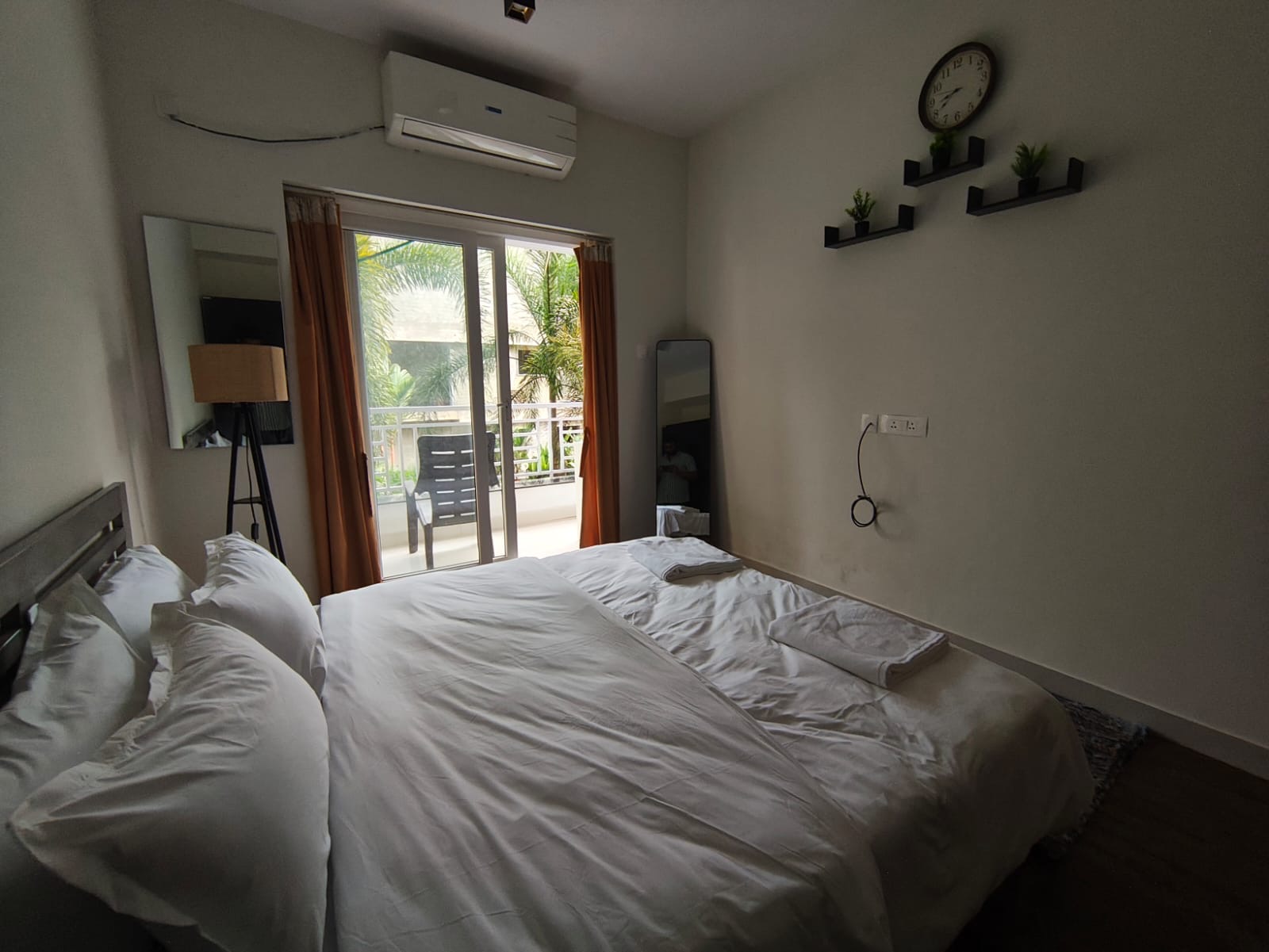 Bedroom with floating shelves, wall clock, and balcony view of palms